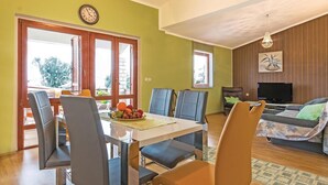 A dining area with a table and chairs, a television in the living room, and a clock on the wall.