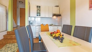 A modern kitchen with white cabinets, a dining table with four chairs, and a fruit bowl on the table.