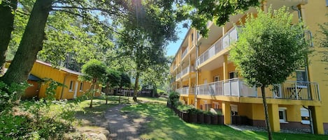 Un sendero conduce a un edificio amarillo con varios balcones, rodeado de árboles y follaje.