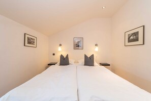 Un lit double avec du linge de lit blanc et deux oreillers, deux tables de chevet avec des lampes et des tableaux encadrés accrochés aux murs.