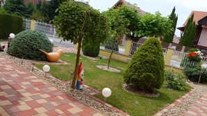 Een tuin met een geplaveid pad, decoratieve bomen en een standbeeld.