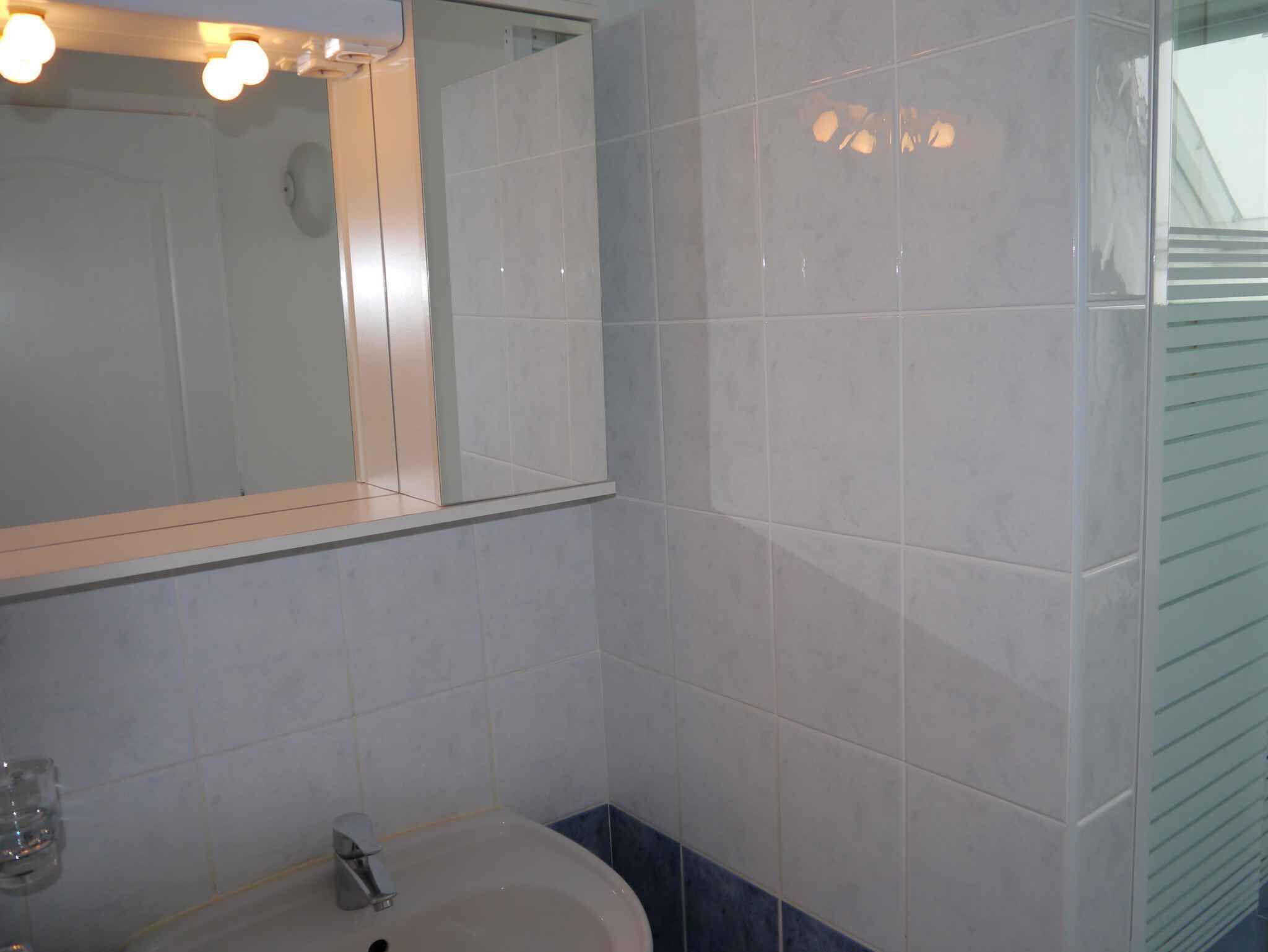 Een badkamer met witte tegels, een wastafel en een spiegel.