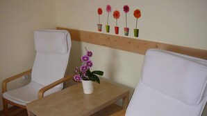 Een kamer met twee witte stoelen, een klein houten tafeltje en een orchidee in pot.