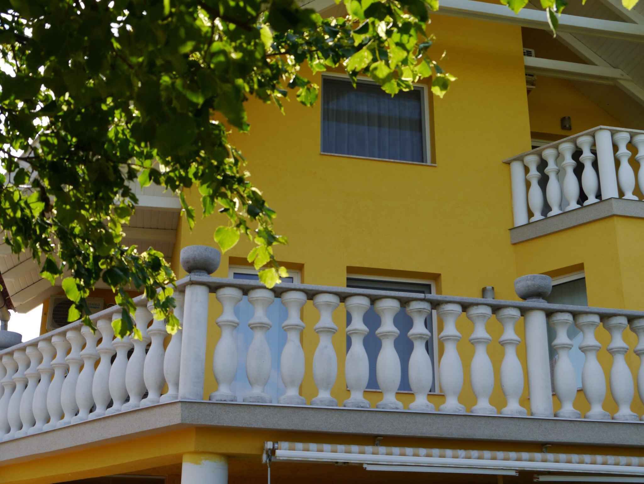Ein gelbes Gebäude mit einem Balkon, der weiße Brüstungen und ein Fenster hat.