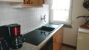Een keuken met een zwart aanrecht, een rode koffiezetapparaat, een dubbele spoelbak en een raam met uitzicht op groen.