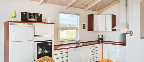 A compact kitchen with white cabinets, a built-in oven, a dishwasher, and a window providing a view of the outdoors.