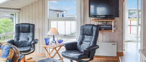A cozy room with two black leather chairs, a small wooden table with a lamp, and a TV mounted on the wall.