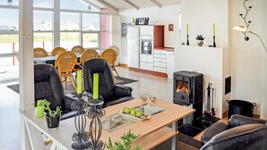 Un soggiorno moderno con un tavolino in vetro, una comoda divisa in pelle nera e poltrone in vimini. Si nota un camino a legna nell'angolo e uno spazio dedicato al dining con un tavolo e sedie bianche.