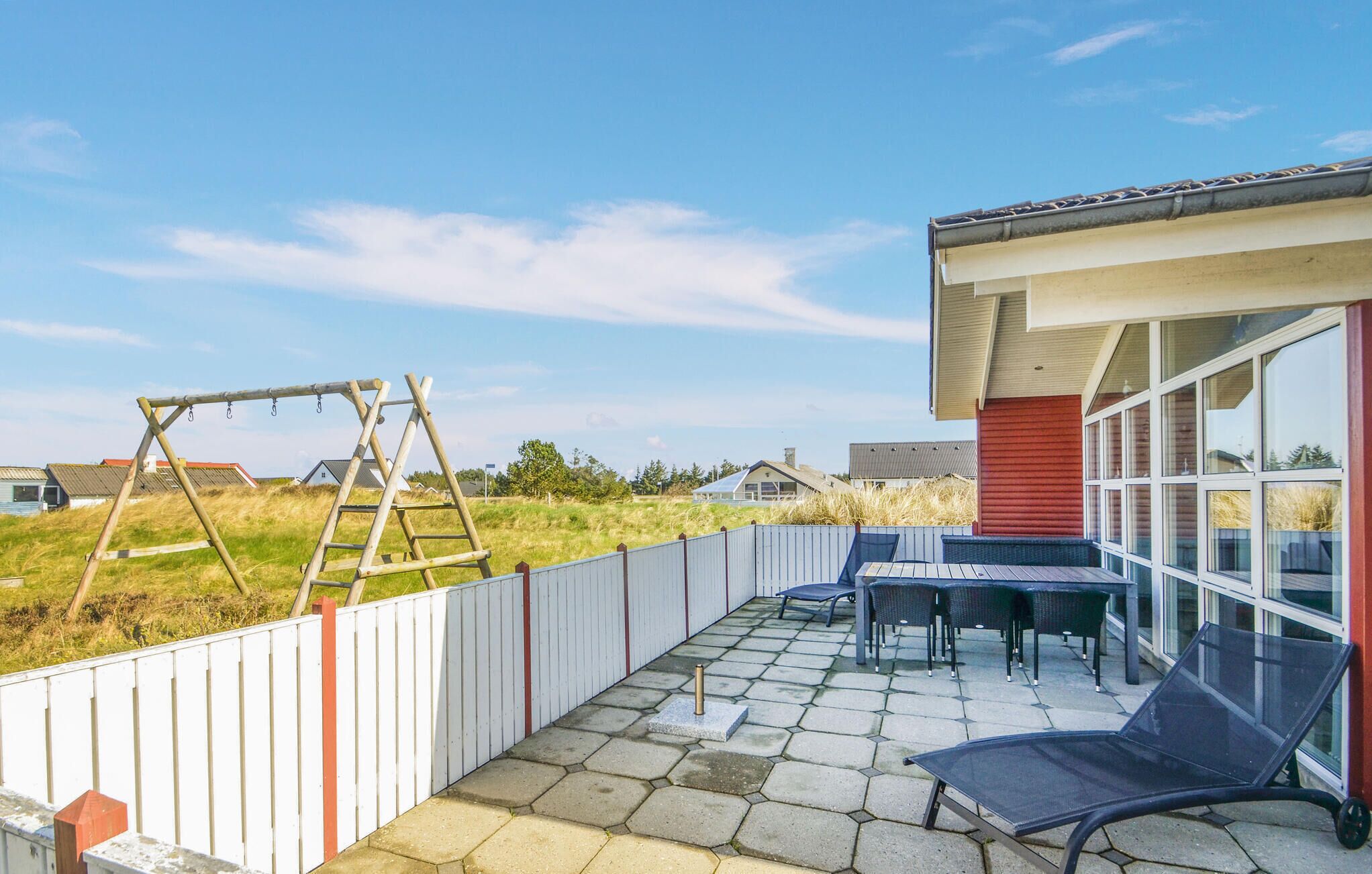 A patio with a swing set, outdoor seating, and a view of houses in the background.