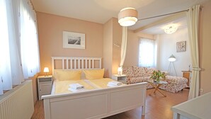 A bedroom with a bed, bedside tables, a chair, a lamp, and a view of another room. - Curr. DG4 - Uns Hüsung (Heringsdorf)
