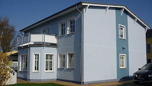 A two-story building with a corner balcony, a garage, and a paved driveway. - Curr. DG4 - Uns Hüsung (Heringsdorf)