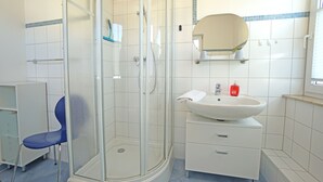 A bathroom with a glass-enclosed shower, a sink with a mirror above it, and a blue chair. - Curr. DG4 - Uns Hüsung (Heringsdorf)
