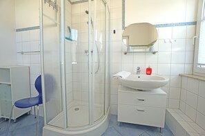Een badkamer met een douchecabine van glas, een wastafel met spiegel erboven en een blauwe stoel.