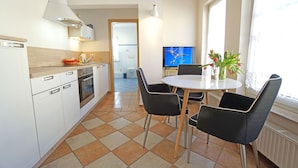 A modern kitchen with white cabinets, a stove, and a dining area with a round table and black chairs. - Curr. DG4 - Uns Hüsung (Heringsdorf)