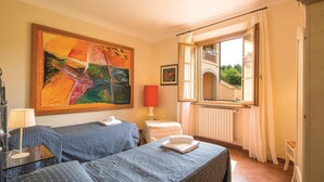A hotel room with two beds, a large abstract painting, a window with a view of a building, and a radiator. - Cozy home in Cerreto Guidi FI with WiFi (Cerreto Guidi FI)