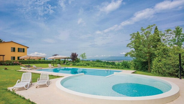 A two-tiered swimming pool with a view of a mountain range, surrounded by a well-maintained lawn and a yellow building. - Cozy home in Cerreto Guidi FI with WiFi (Cerreto Guidi FI)