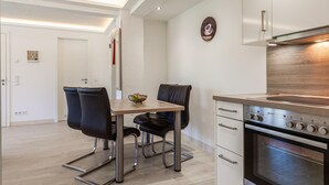 A modern kitchen with a built-in oven, a dining table with chairs, and a wall-mounted clock.