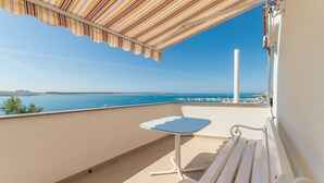 Ein Balkon mit gestreiftem Sonnensegel, einer weißen Bank und einem kleinen Tisch.