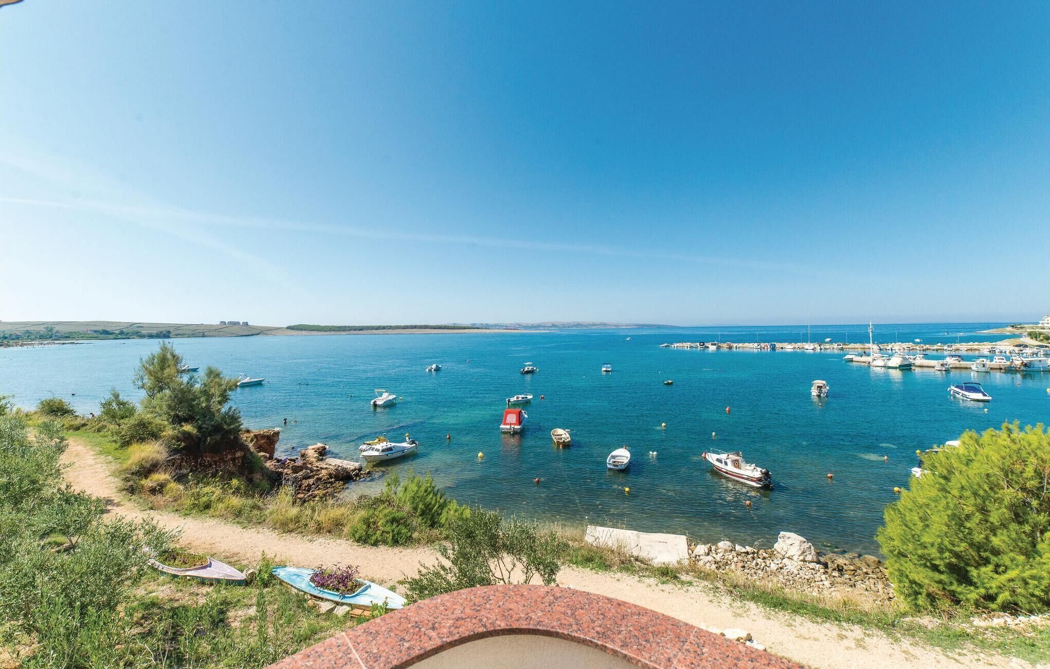A coastal view with boats docked at a marina, a sandy beach, and a clear blue sky.