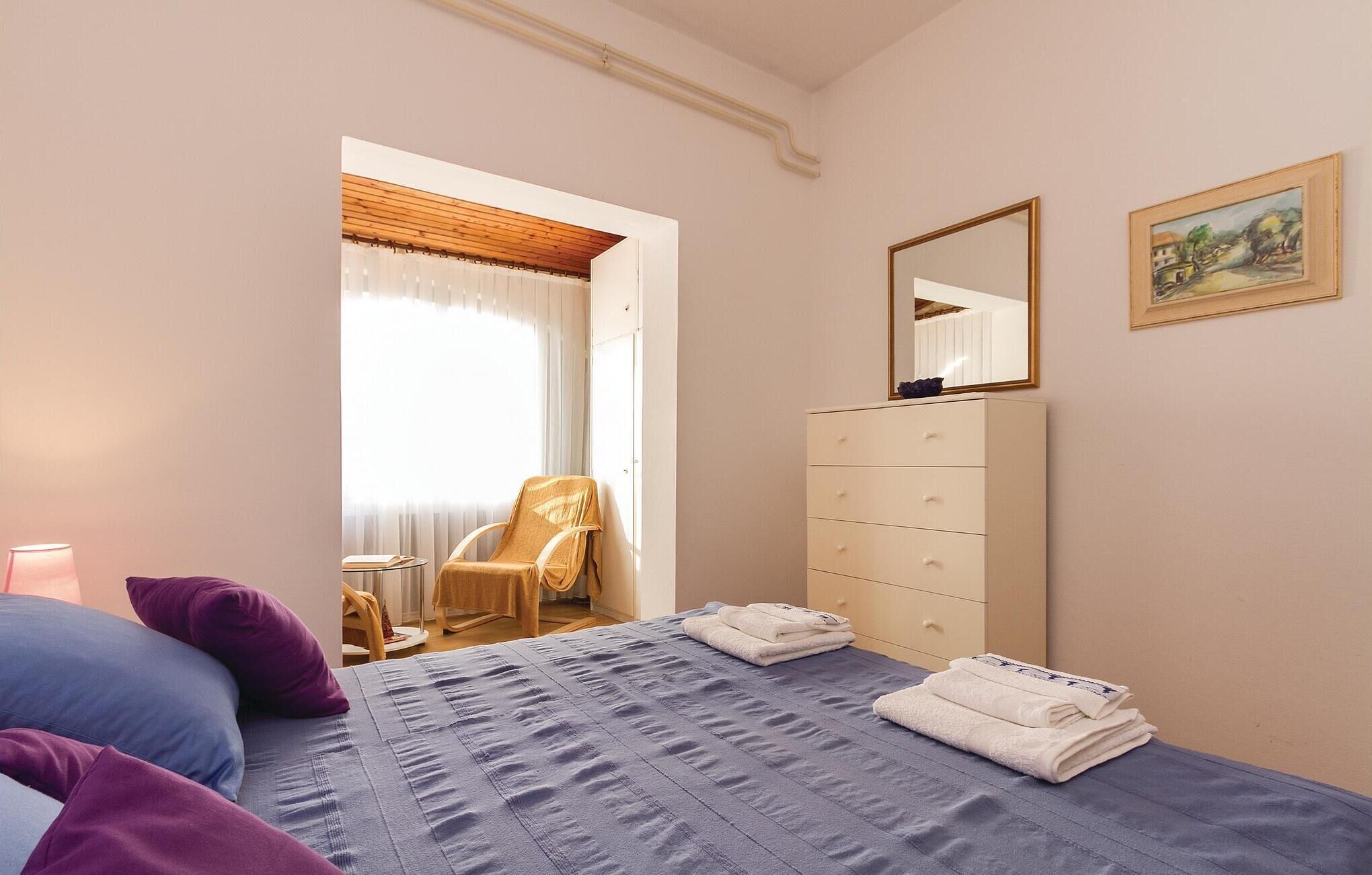 Une chambre à coucher avec un lit, une commode, une chaise et un tableau accroché au mur.