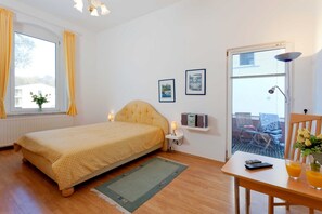 A bedroom with a bed, a small table with a remote control, a glass of orange juice, and a window with curtains.