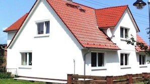 Een huis met twee verdiepingen, een rode dakbedekking en witte muren.