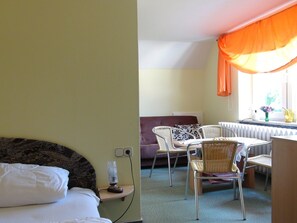 A hotel room with a bed, a small table with chairs, a radiator, and a window with curtains. - Apartment 35 - Apartments on Usedom (Rankwitz)