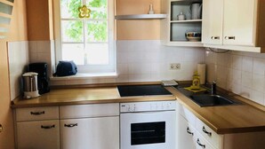 Eine Küche mit weißen Schränken, einem Fenster mit Blumendekoration, einer Kaffeemaschine und einem Spülbecken.