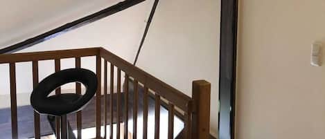A staircase with a wooden railing, a black chair, and a flat-screen TV mounted on the wall.