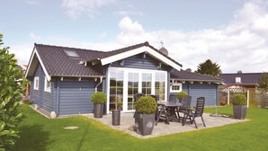 A two-story house with a large glass door entrance, a patio with a table and chairs, and a well-maintained lawn. - Stunning home in Rønde with kitchen (Rønde)