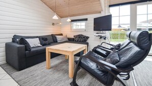 A cozy living room with a sofa, a coffee table, and a leather chair. A flat-screen TV is mounted on the wall, and there is a window providing a view of the outdoors. - Stunning home in Rønde with kitchen (Rønde)