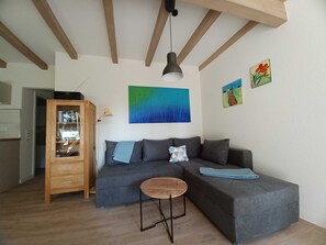 A modern living room with a grey sofa, a wooden cabinet, a round wooden table, and a ceiling with exposed beams.