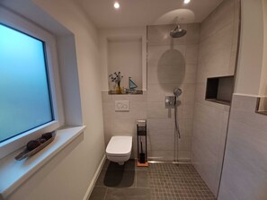 A modern bathroom with a toilet, shower, and a window.