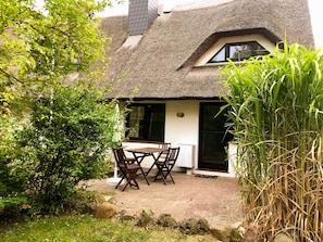 Een vakantiehuisje met rieten dak, een patio tafel en stoelen, omringd door groen.