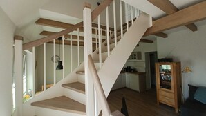 Una escalera con vigas de madera y barandillas blancas que lleva a una zona de cocina con armarios y una cafetera.
