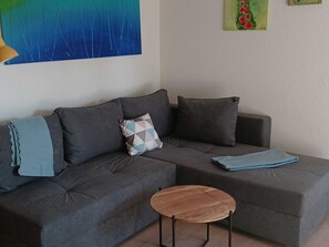 Een moderne woonkamer met een hoekbank, een ronde salontafel en een decoratief kussen.