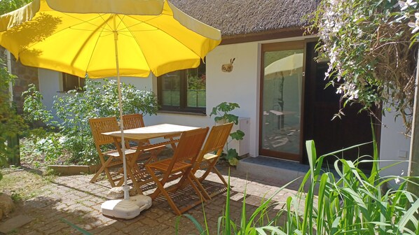 A patio with a table and chairs, a yellow umbrella, and a house with a thatched roof.