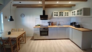 Una cocina moderna con vigas de madera, horno empotrado, un lavamanos y armarios blancos.