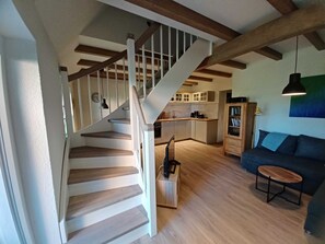 A staircase leading to a kitchen with wooden beams, a sofa, and a small table.