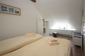 A bedroom with two beds, a window, a radiator, and a small cabinet.