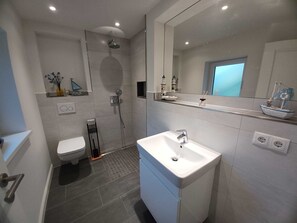 A modern bathroom with a shower, toilet, and sink, featuring a large mirror and decorative items.