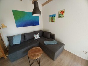 A modern living room with a grey sectional sofa, a round wooden coffee table, and two wall-mounted paintings.