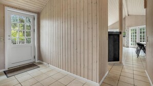 Corredor com painéis de madeira, porta branca com painéis de vidro e piso revestido de azulejos.