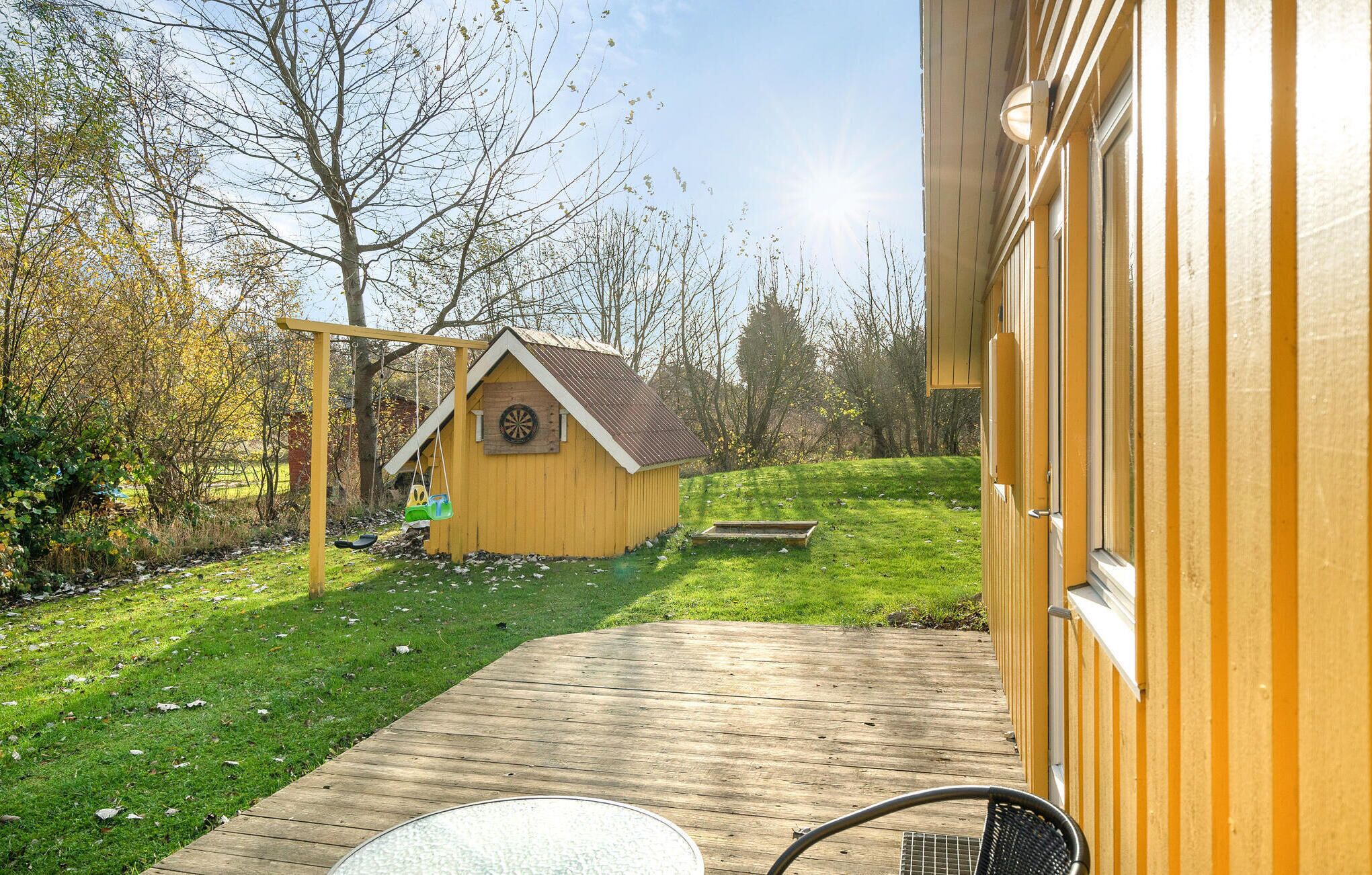 A wooden deck leading to a small wooden structure with a sloped roof, a dartboard, and a swing set.