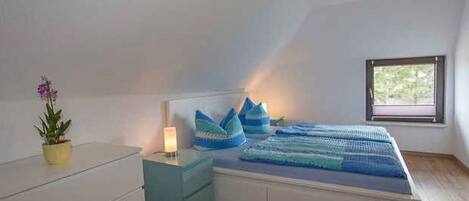 A bedroom with a bed, bedside table, lamp, and a window.