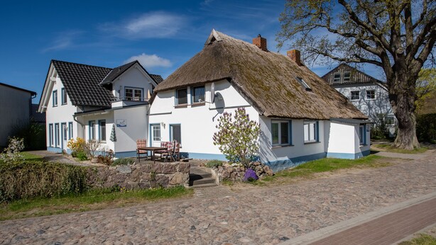 Ein traditionelles Haus mit einem Strohdach, einem Steinweg und einer Bank davor.