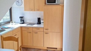 Een compacte keuken met houten kastjes, een magnetron, een klok en een koffiezetapparaat.