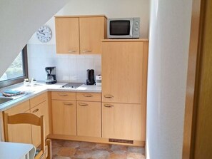 Cocina compacta con armarios de madera, microondas, un reloj y cafetera.