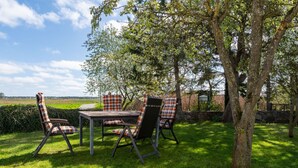 Een terras met een tafel en vier stoelen, omringd door gras en bomen.