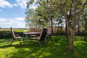 An outdoor dining area with a table and four chairs, surrounded by grass and trees.